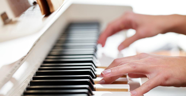 Um homem aprendendo a tocar piano online com um computador em casa